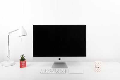 银色iMac、苹果无线键盘和靠近台灯的苹果魔术触控板